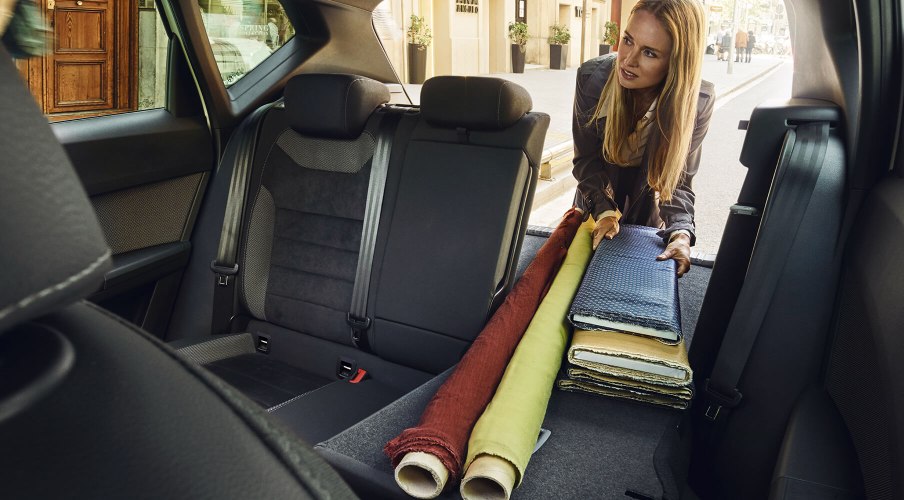 SEAT neuer Service und Wartung – Pannenhilfe – Frau legt Gegenstände auf den Rücksitz eines Fahrzeugs, die Sitze sind für mehr Platz umgeklappt