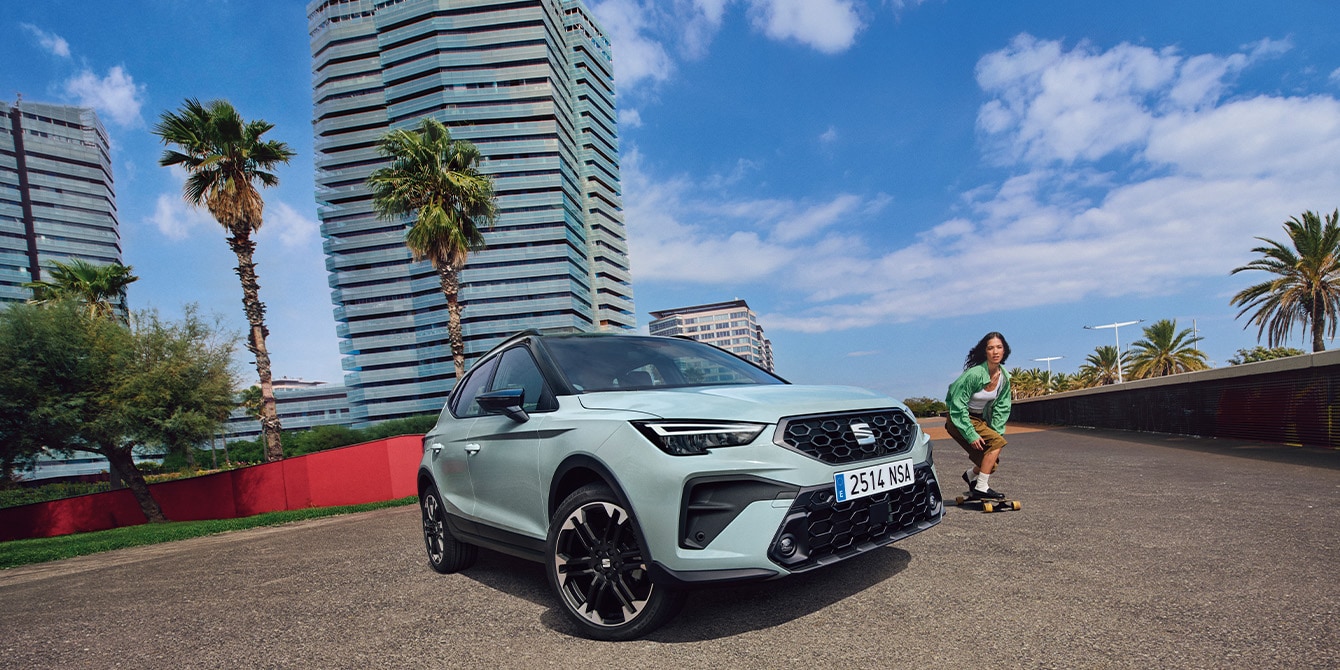 SEAT Arona, geparkt auf einer sonnigen Strasse mit modernen Stadtgebäuden und einem vorbeifahrenden Skater.
