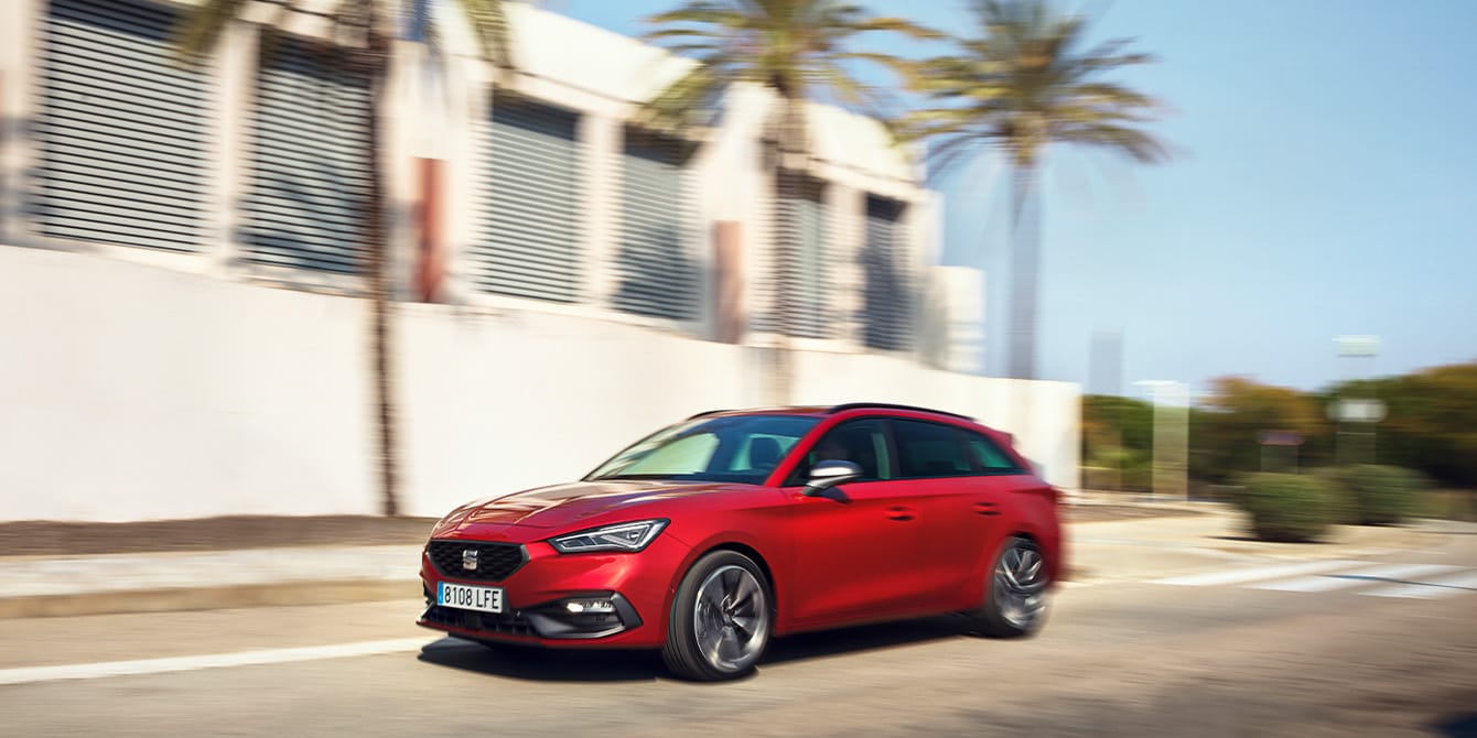Roter SEAT Leon Sportstourer in Bewegung in einem Wohngebiet mit einem Haus und Palmen.