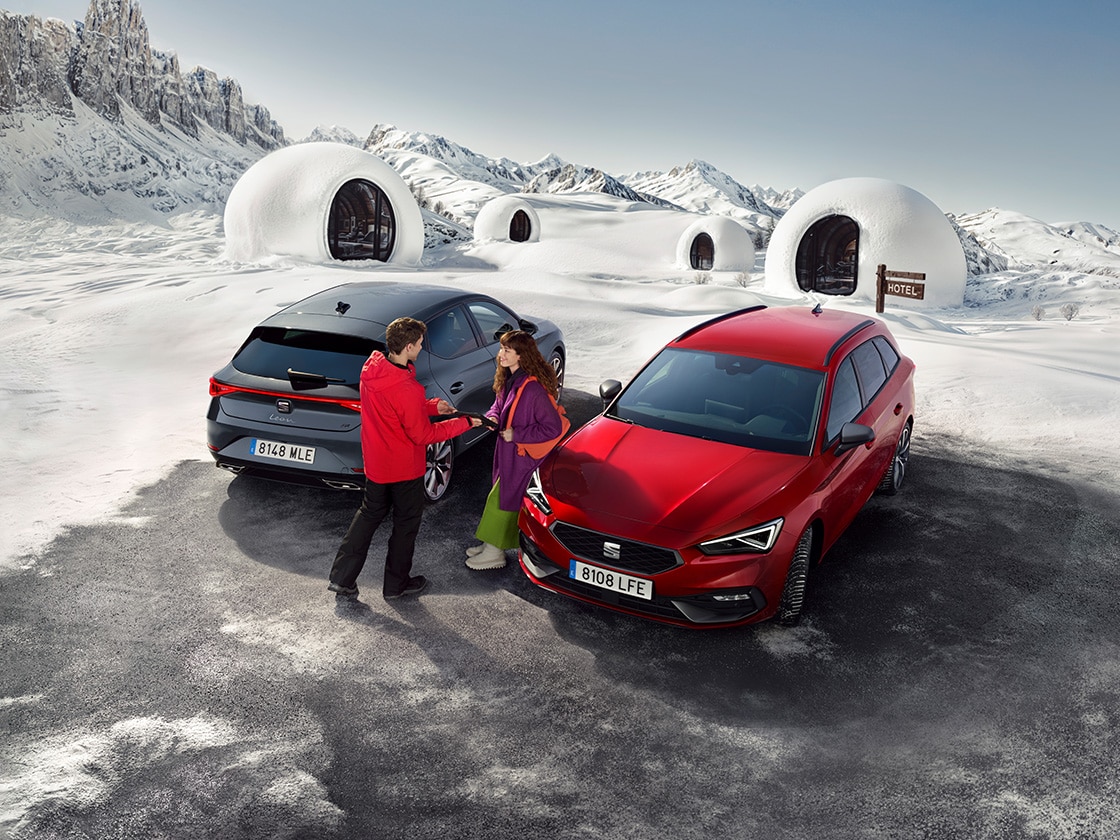 Ein Paar unterhält sich neben einem SEAT Leon in Desire Red in einer verschneiten Berglandschaft