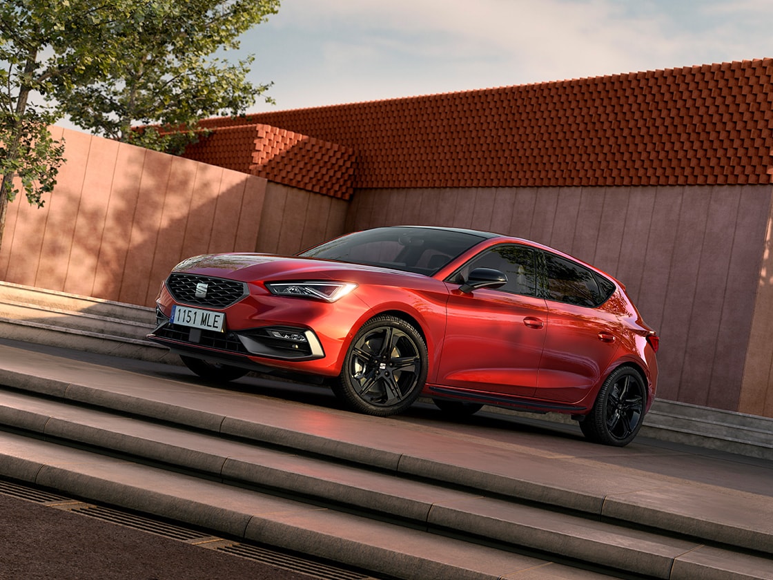 Ein Paar unterhält sich neben einem geparkten SEAT Leon in Desire Red
