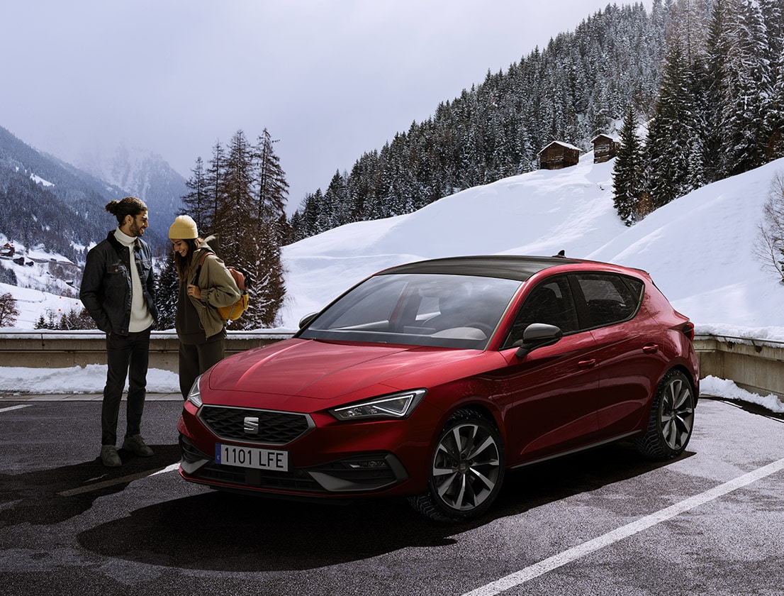 una coppia parla accanto a una seat leon in desire red su una montagna innevata