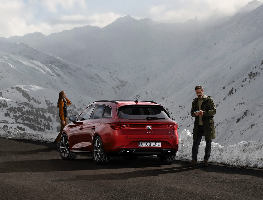 vista posteriore di una seat leon in desire red mentre una coppia ammira le montagne