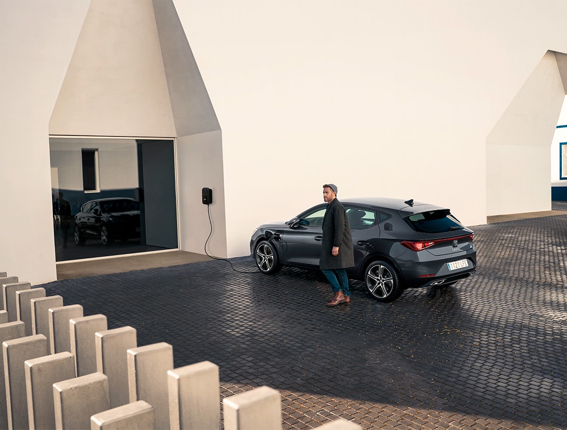 un uomo si allontana dalla seat leon e-hybrid in desire red con in mano il suo smartphone