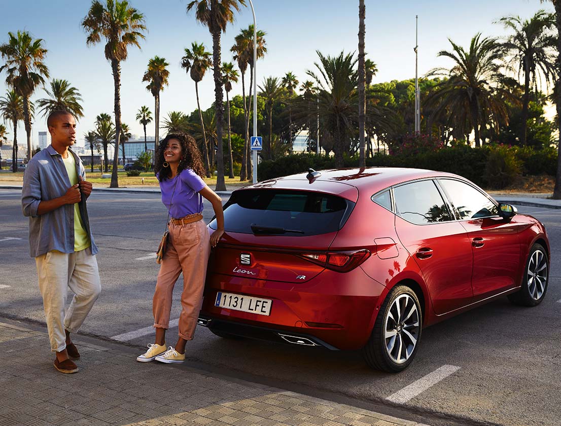 Ein Paar unterhält sich neben einem geparkten SEAT Leon in Desire Red