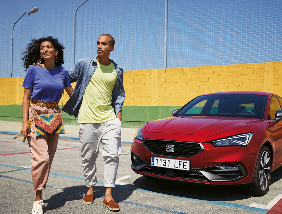 Ein Paar unterhält sich neben einem geparkten SEAT Leon in Desire Red