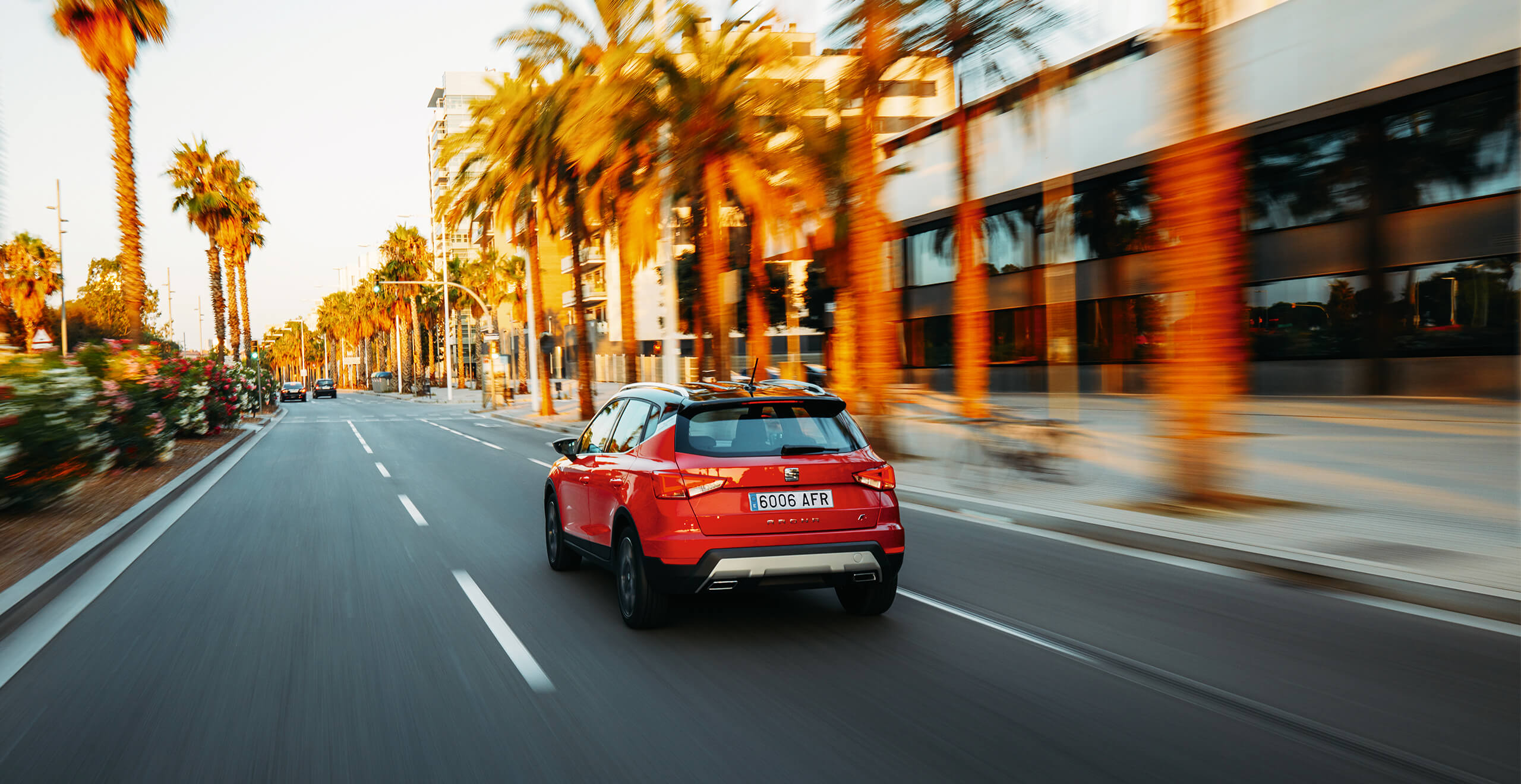 SEAT Arona crossover SUV driving in an urban street lined with palm trees