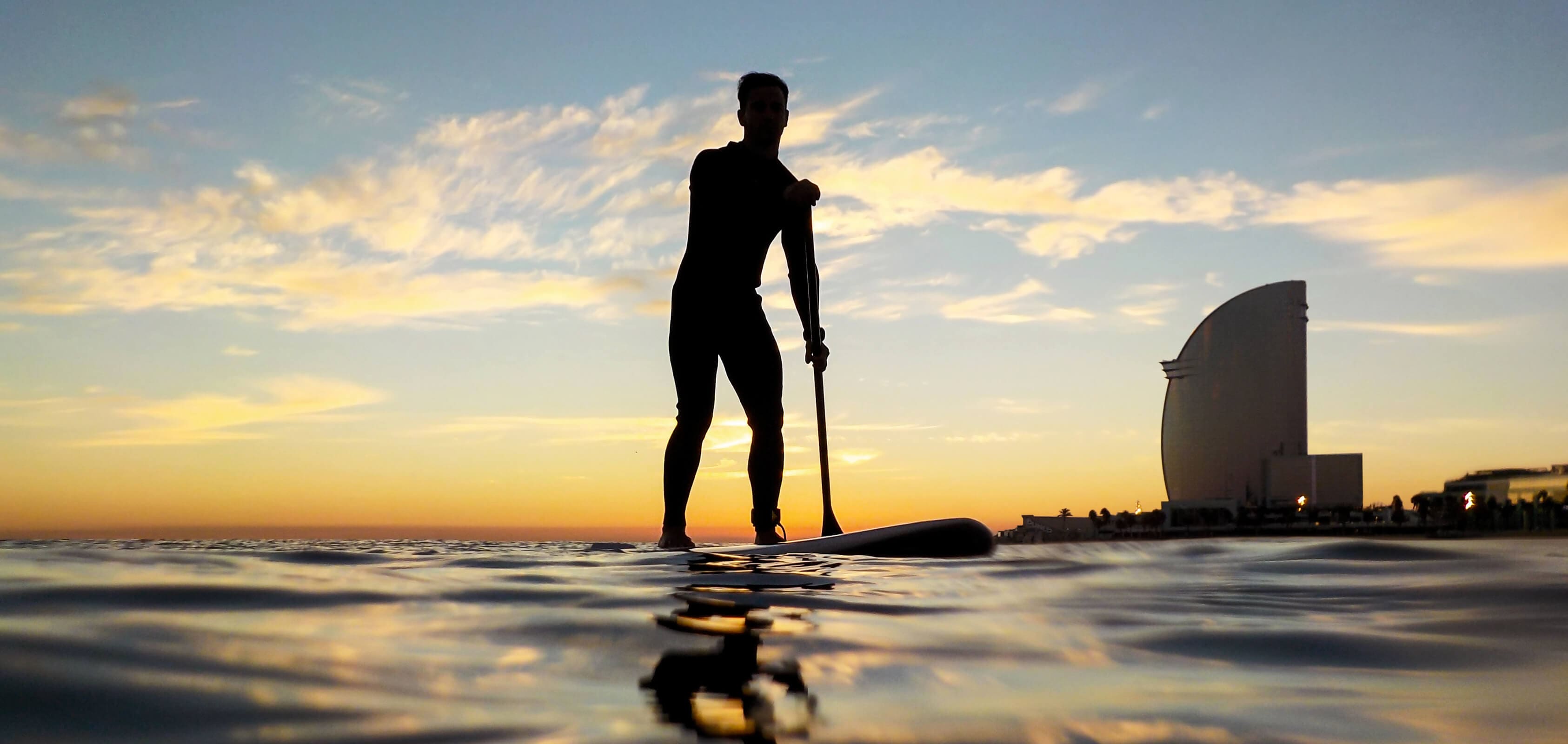 Silhouette d’un homme nageant sur une planche de surf à la plage de Barceloneta, avec le W hotel en arrière-plan