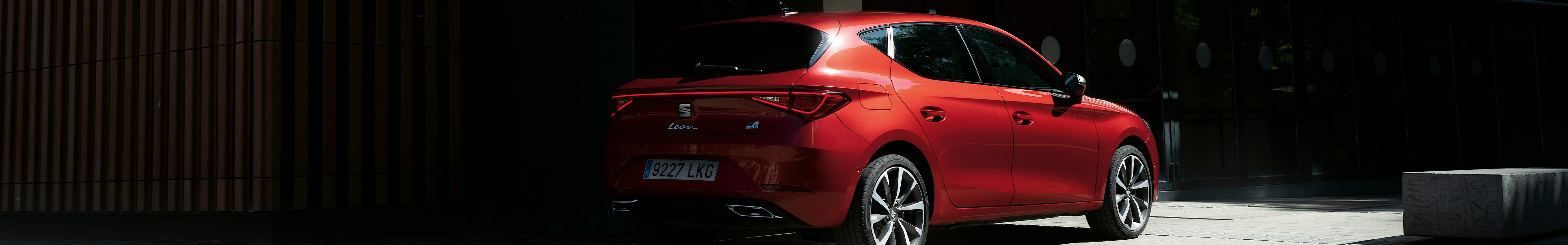 Sedile per veicoli elettrici mild hybrid leon sportstourer di colore rosso parcheggiato all’ombra di un edificio