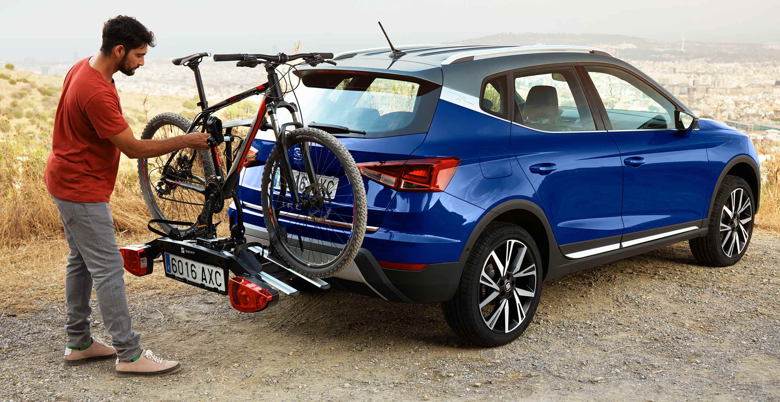 SEAT neuer Service und Wartung – Mann stellt ein Fahrrad auf den Fahrradträger am Heck eines SEAT Arona Crossover