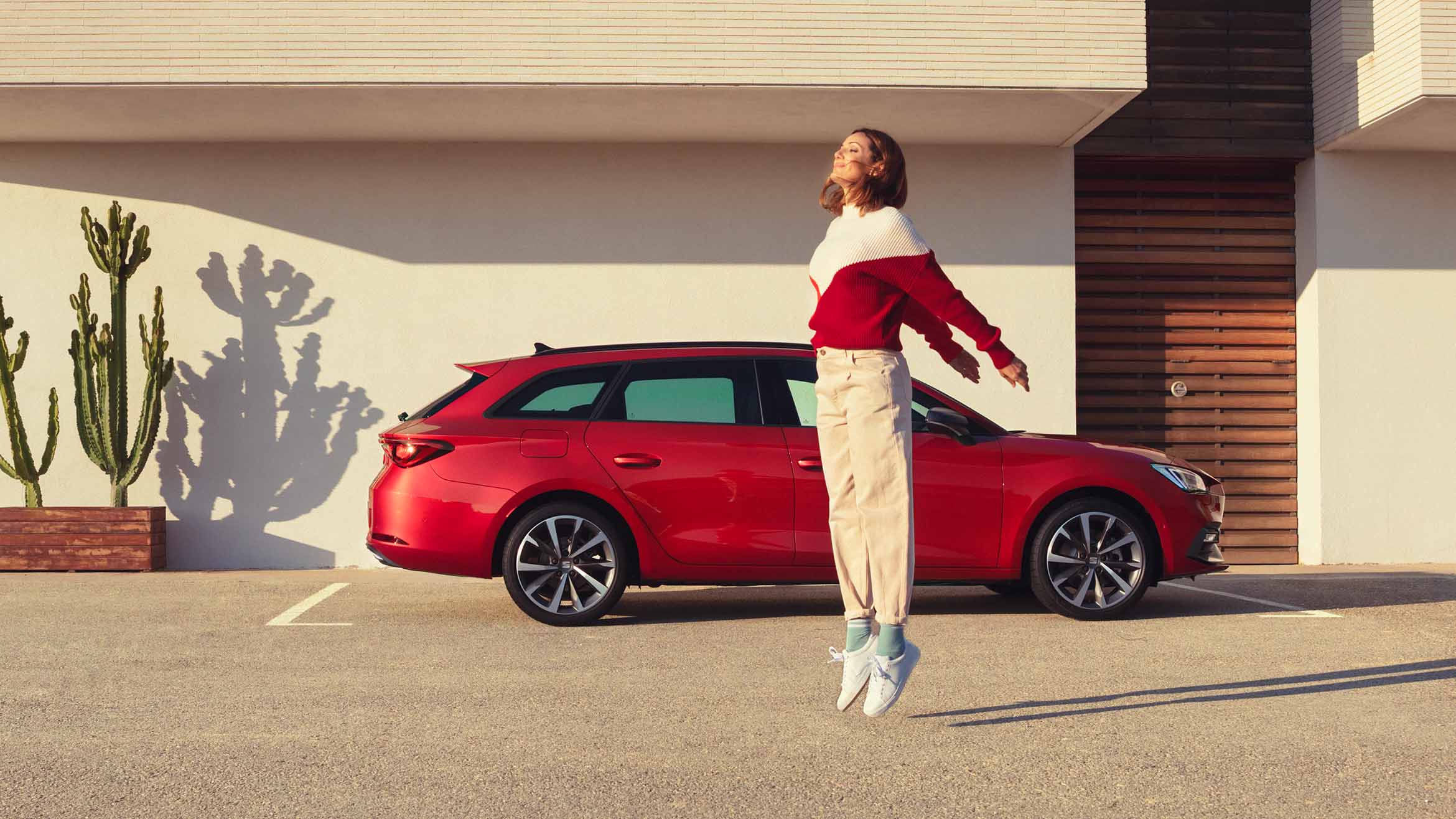 donna che salta accanto a una seat leon sportstourer in desire red