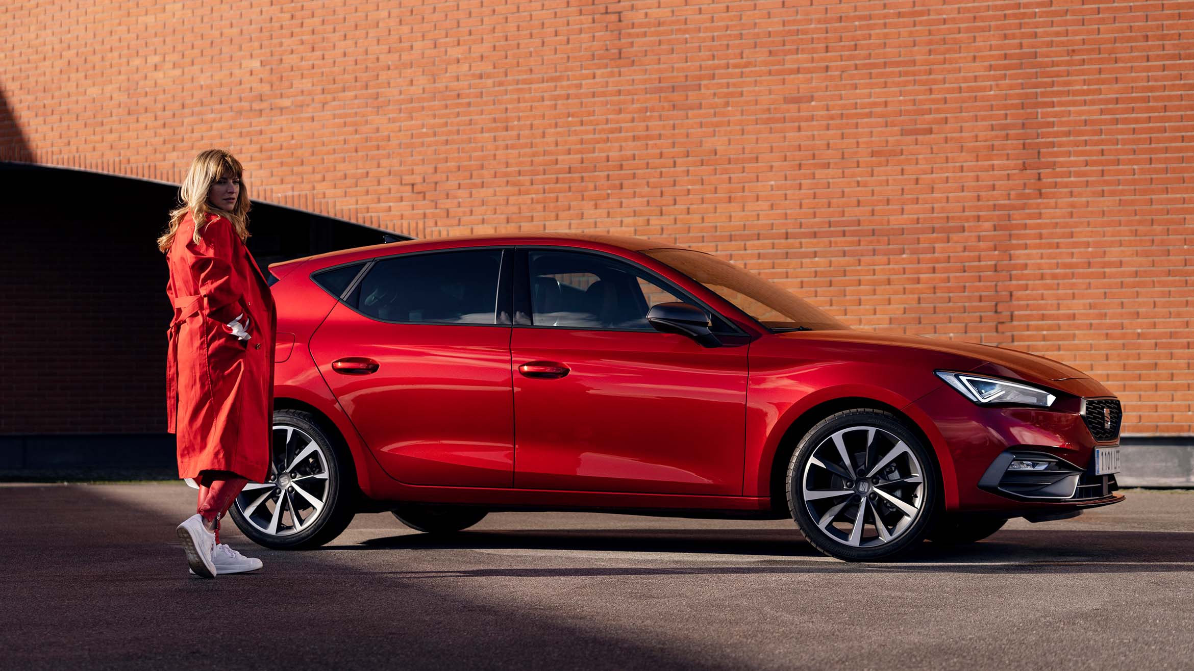 donna con cappotto rosso in piedi accanto a una seat leon in desire red