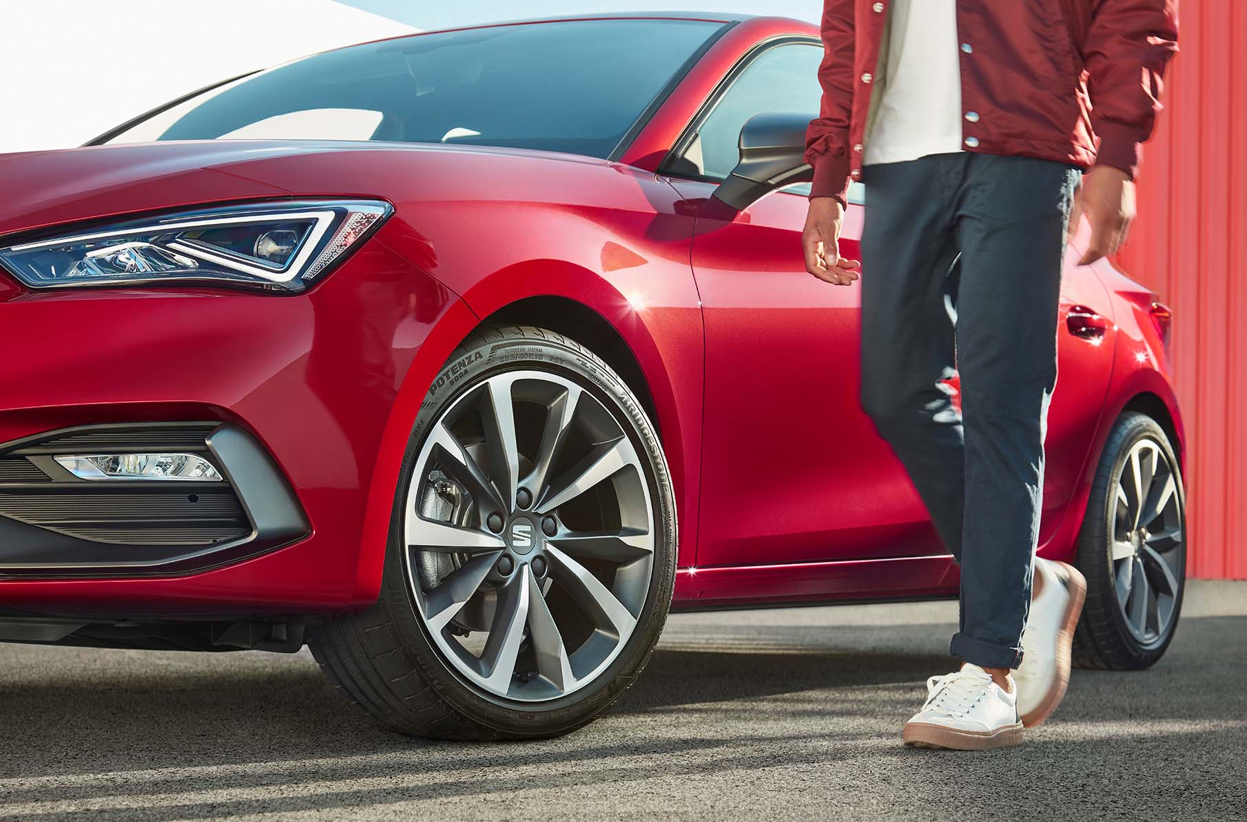 uomo in piedi accanto a una seat leon in desire red con cerchi in lega leggera in cosmo grey