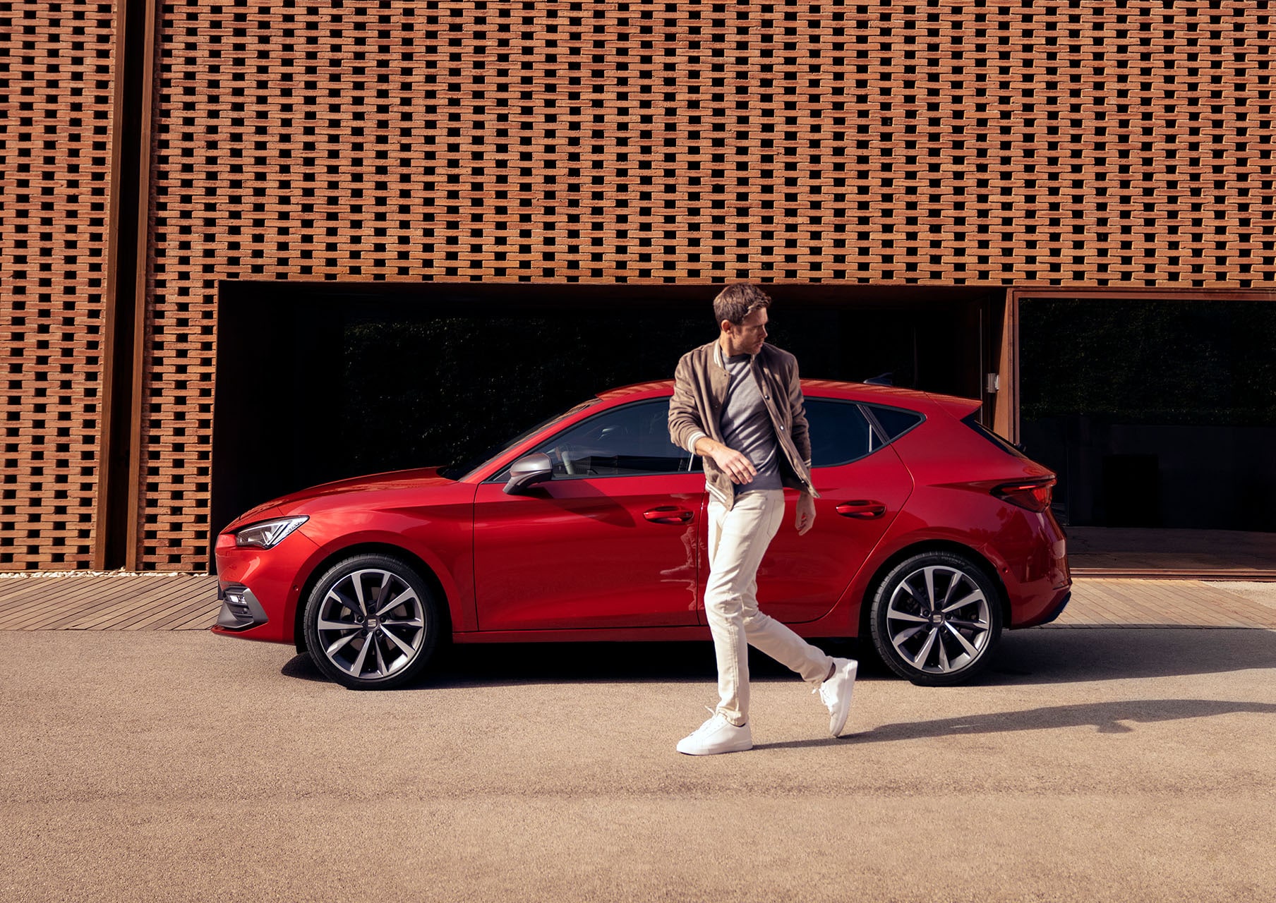 un uomo cammina accanto a una seat leon in desire red con cerchi in lega leggera  