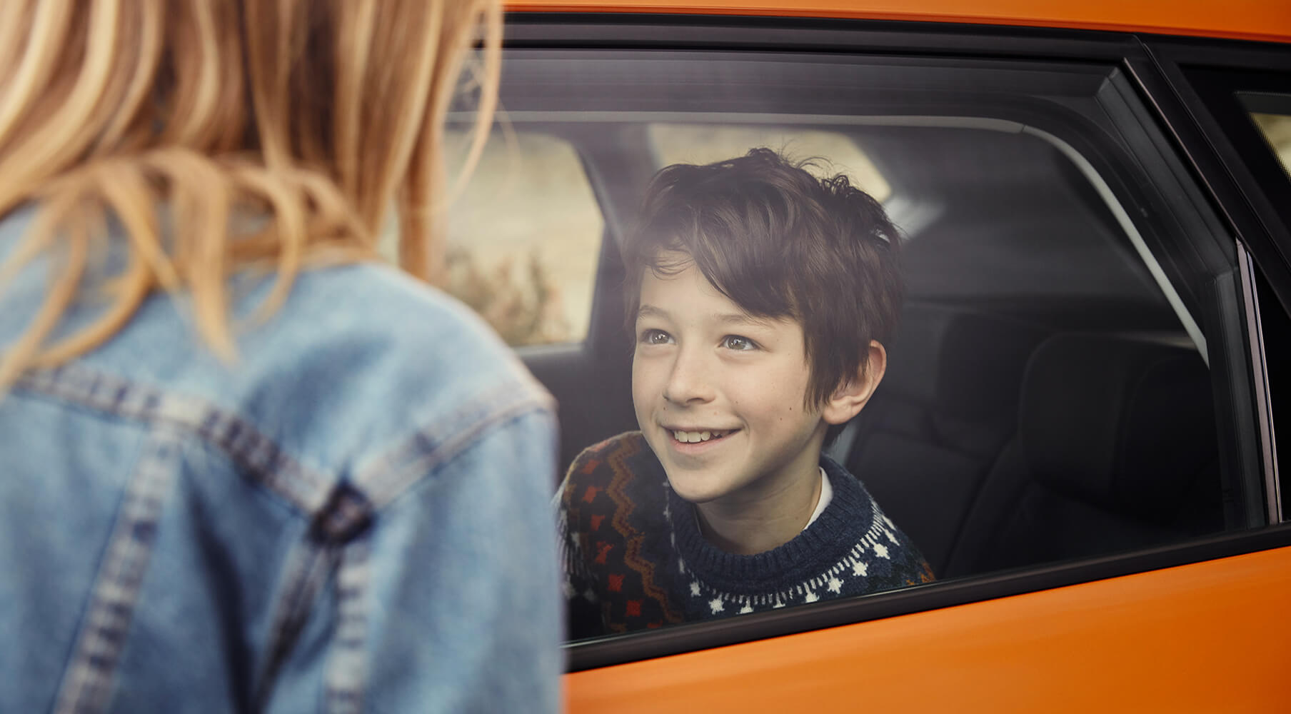 SEAT neuer Service und Wartung – Pannenhilfe –Seitenansicht eines Knaben in einem neuen Fahrzeug, der einer Frau, die draussen steht, zulächelt.