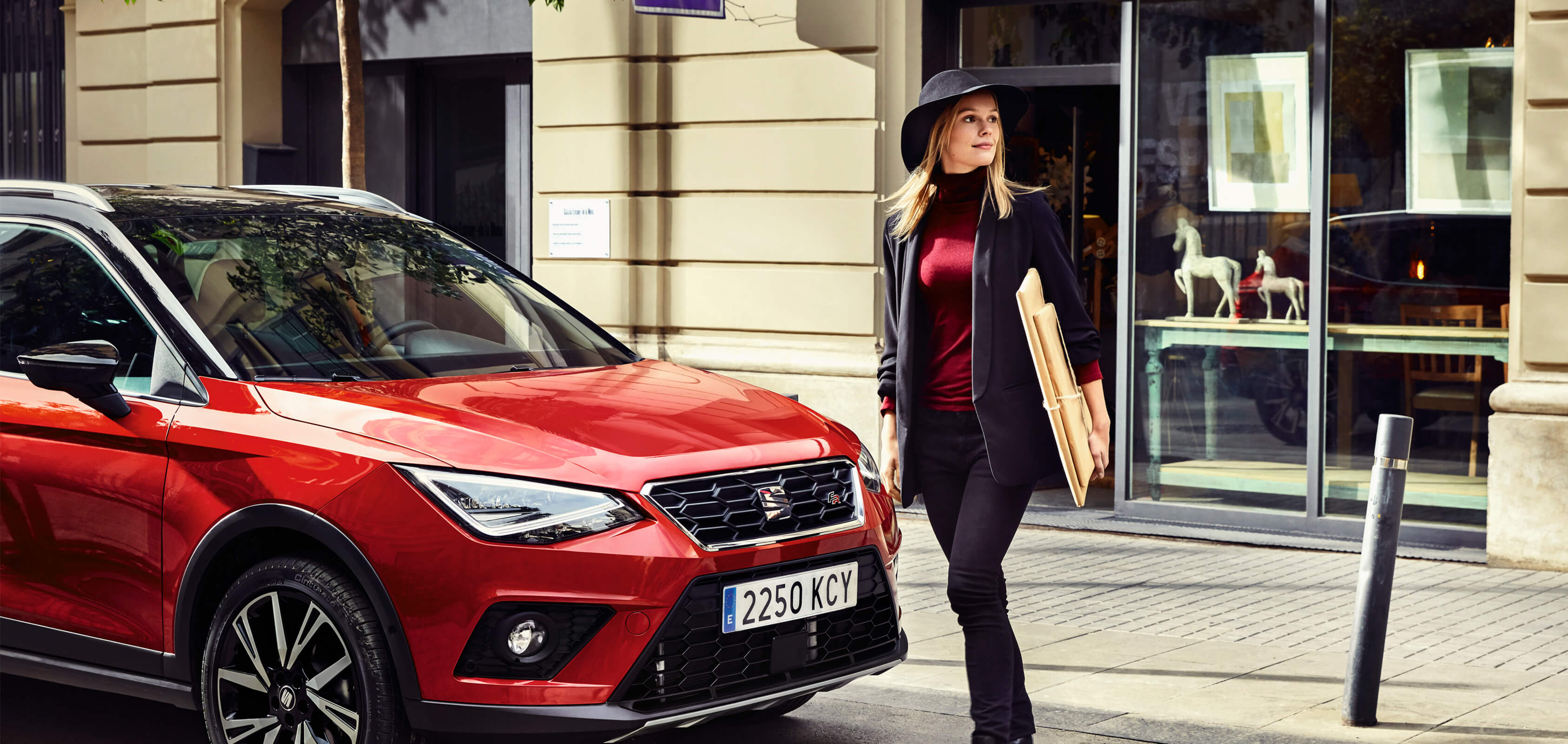 SEAT servizi auto nuove manutenzione controlli revisione – una donna cammina davanti a un SUV crossover SEAT Arona rosso